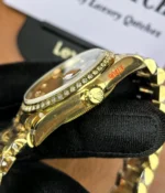 Close-up view of the crown on the Rolex Day-Date M128348RBR-0035 with a green dial, gold Oyster strap, and diamond bezel for women.