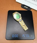 Display showing the weight of the Rolex Day-Date M128348RBR-0035 with a green dial, gold Oyster strap, and diamond bezel for women.